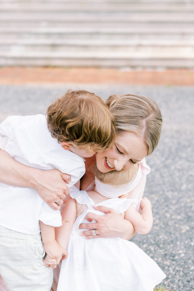 Mother Kneeling And Hugging Her Two Young Children