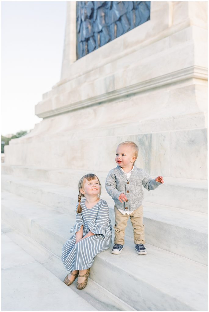 A Big Sister Looking Up At Her Little Brother During A Family Photography Session.