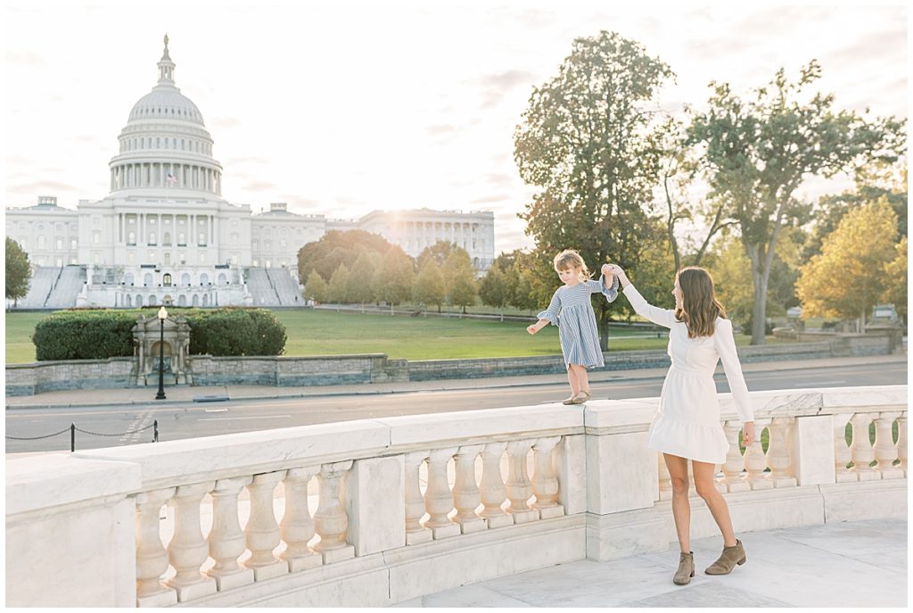 Mother Walking Her Daughter On A Railing In Front Of The Capitol Building In Dc