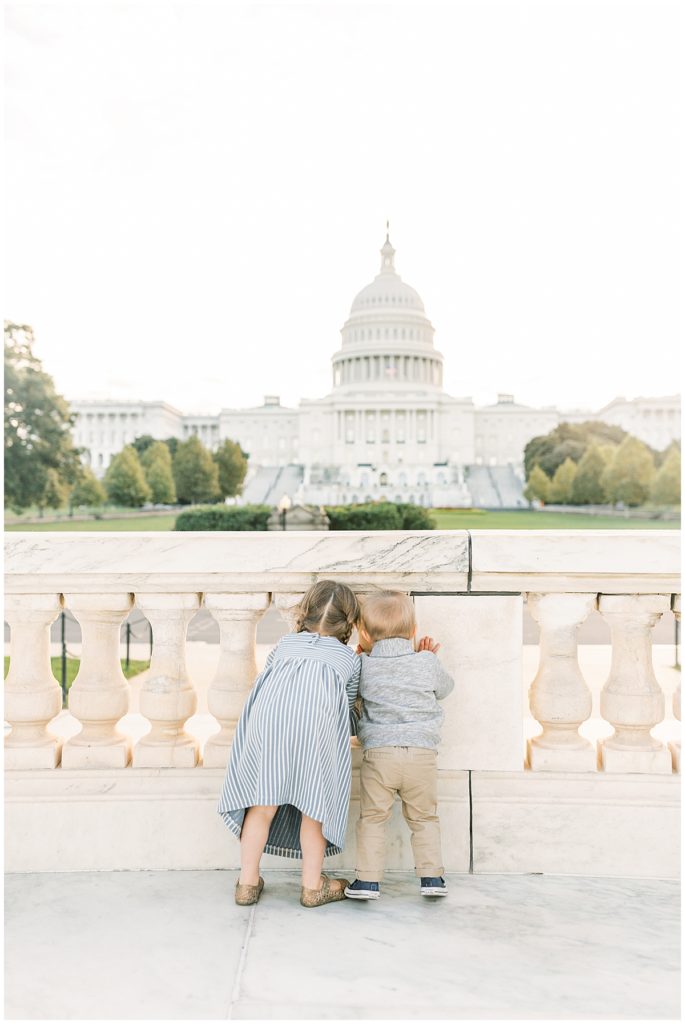 A Young Girl And Boy Looking Through A Railing At The Us Capitol.