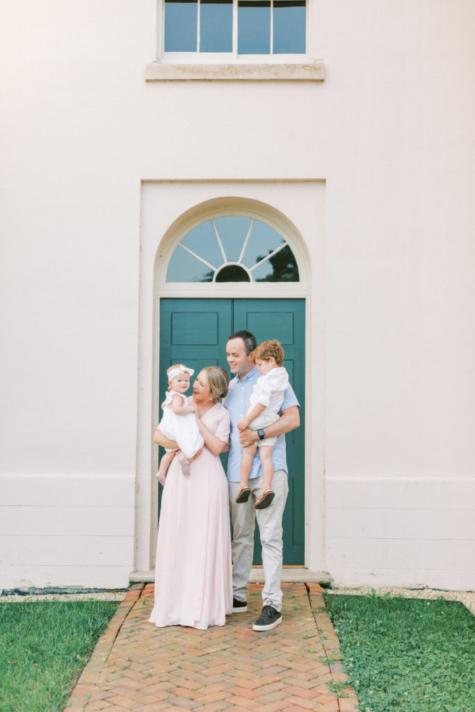 Young Family Standing In Front Of Green Doors During A Timeless Maryland Family Session.