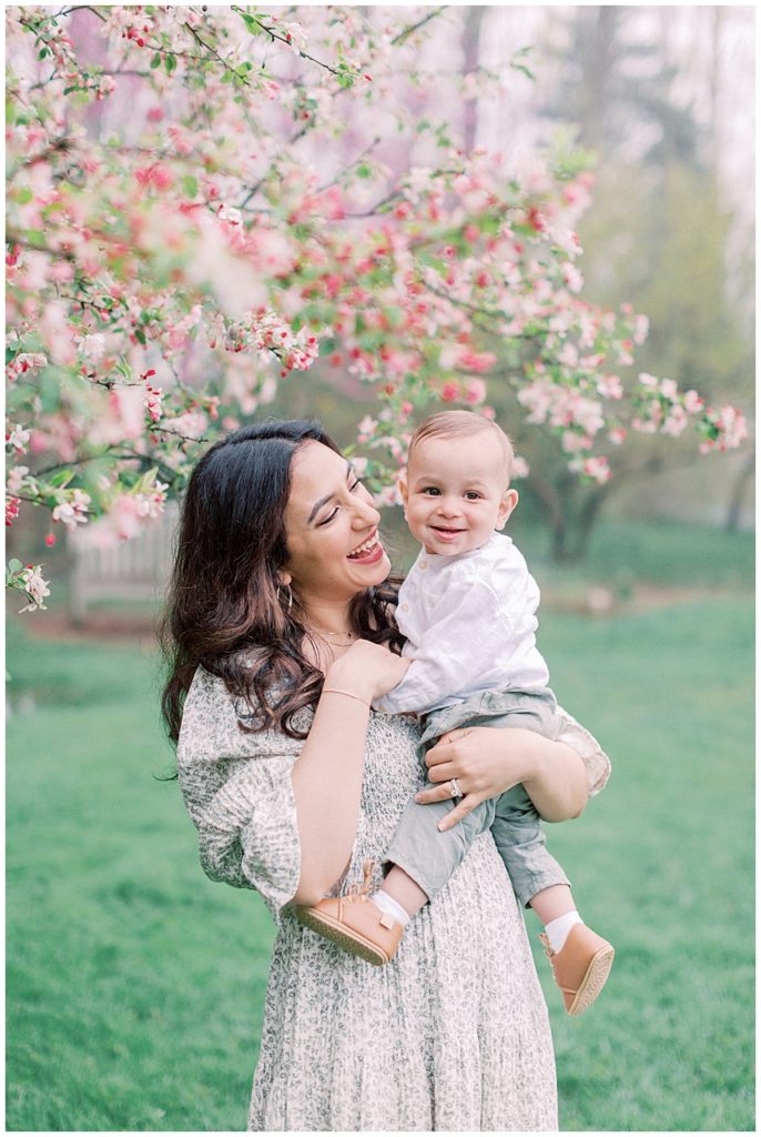 Mother Holds Her Son Next To Cherry Blossom Tree In Brookside Gardens In Maryland.