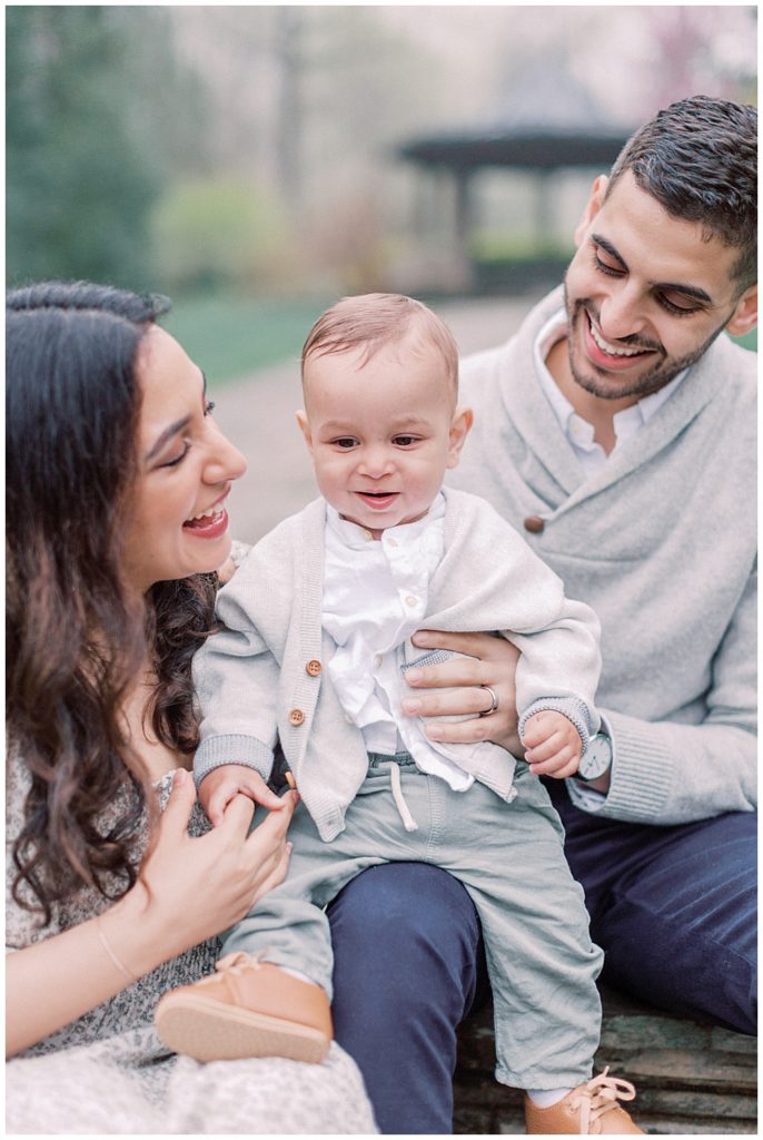 Mother, Father, And Baby Sit In A Park.