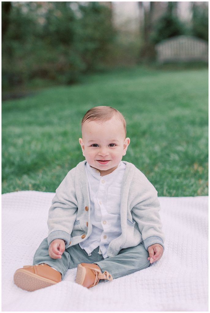 Young Baby Boy Sits On A Blanket In A Park.