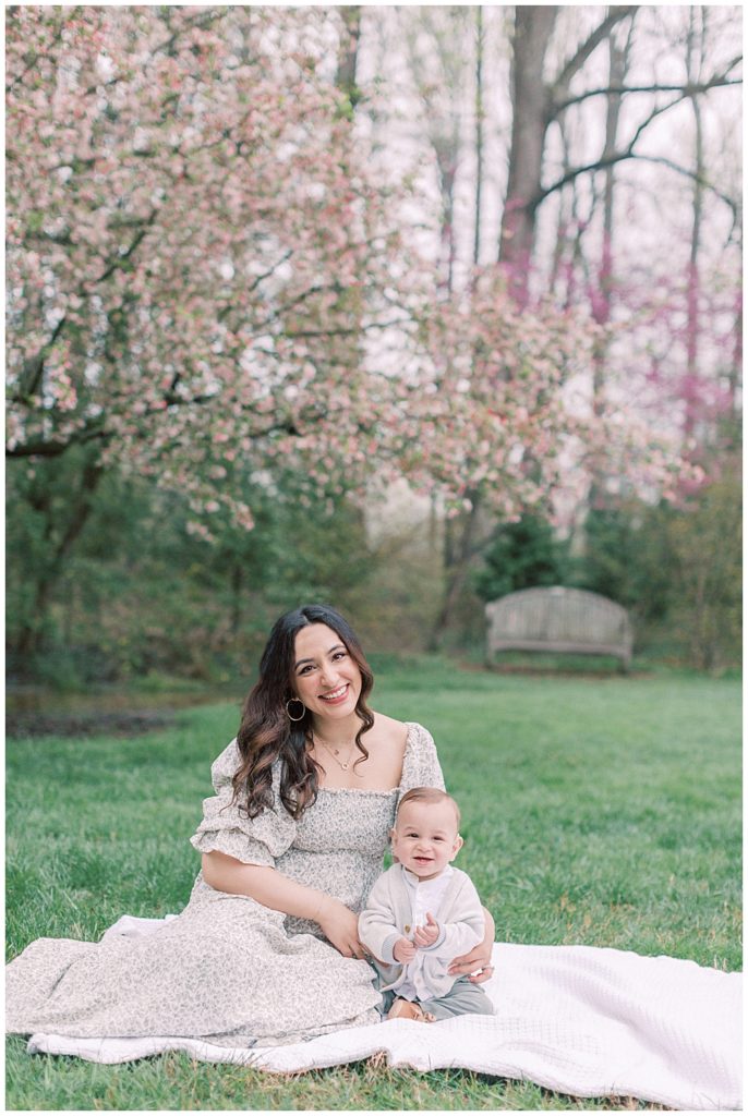 Mother Sits Next To Her Young Son On A Blanket By A Cherry Tree.