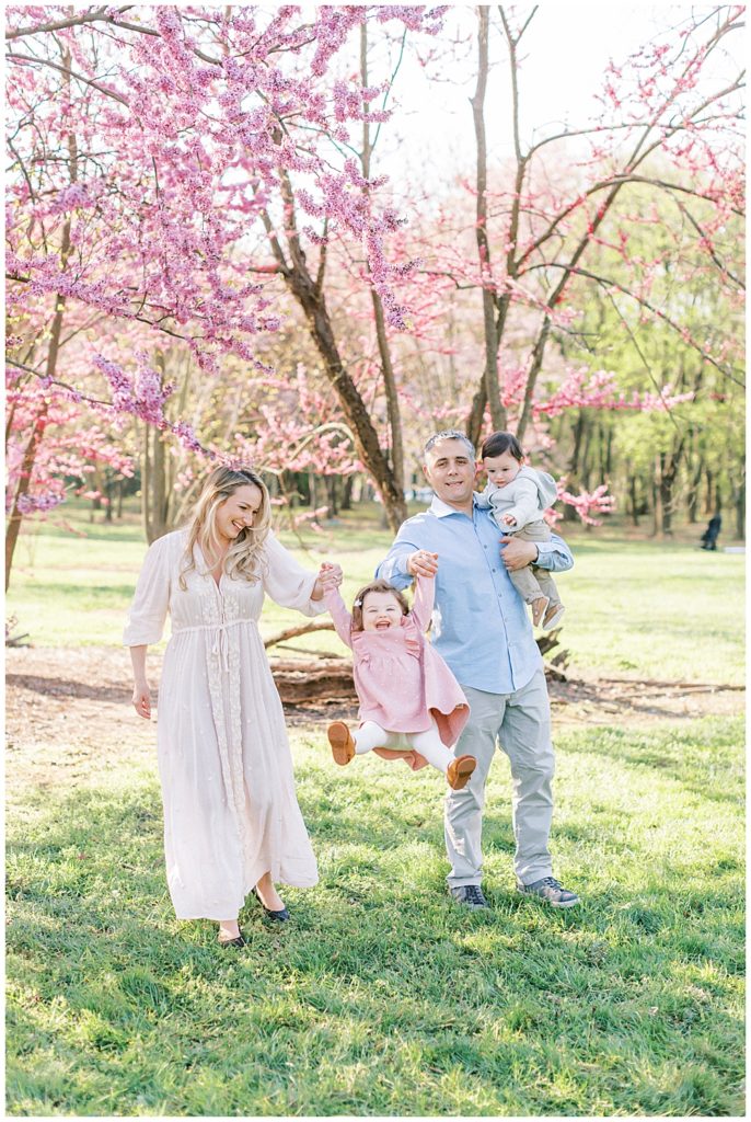 Mom And Dad Walk With Their Two Kids, Swinging Their Toddler Daughter