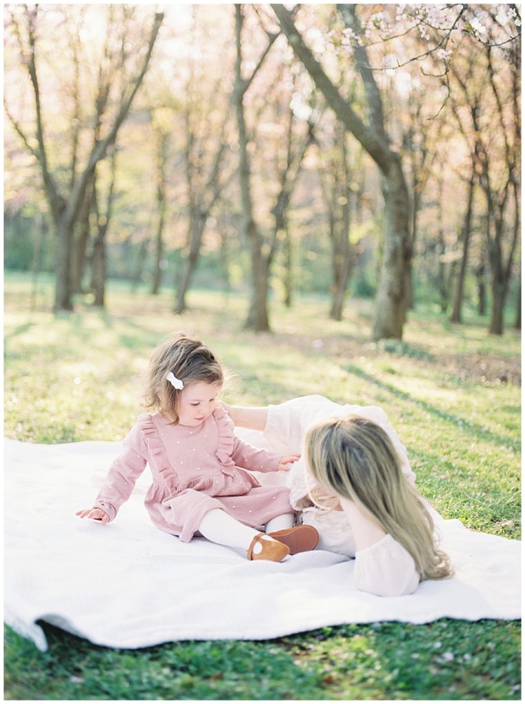 Mother Lays On A Blanket With Her Toddler Daughter At The National Arboretum In Washington, D.c.