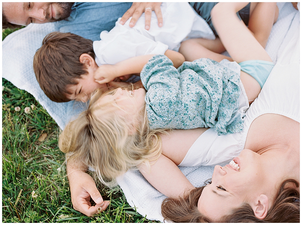 Family Laughs And Lays Down Together On A White Blanket