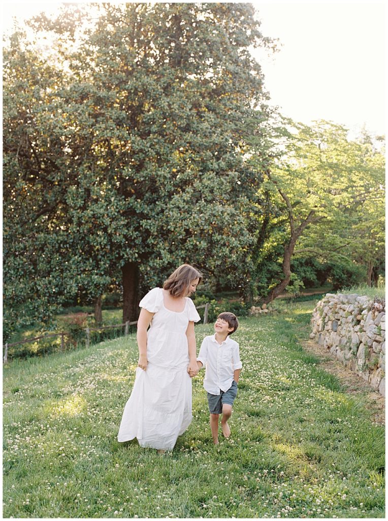 Mother And Her Son Walk Through A Field During Sunset