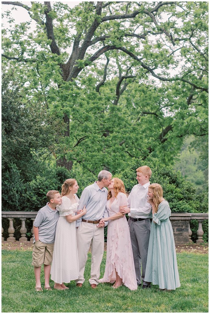 Mother And Father Kiss While Standing With Their Grown Children At Glenview Mansion In Maryland