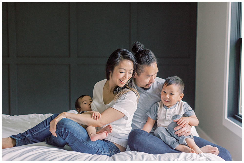 Family Sits On A Bed And Smiles At Their Son