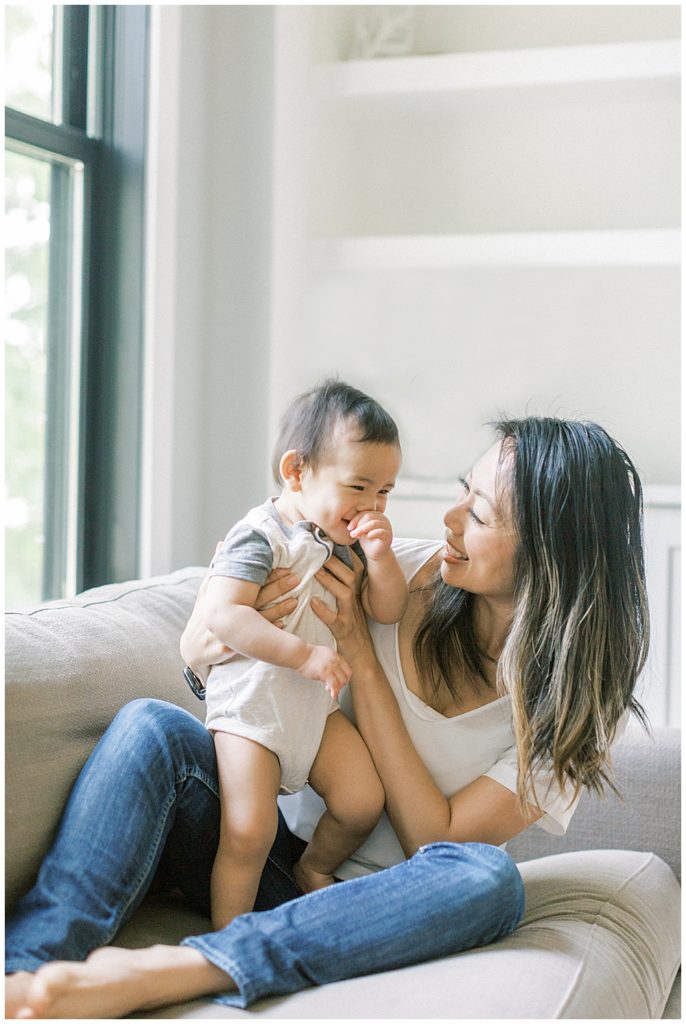 Mother Holds Up Her Infant Son While Sitting On A Couch During Her Northern Virginia In-Home Family Session