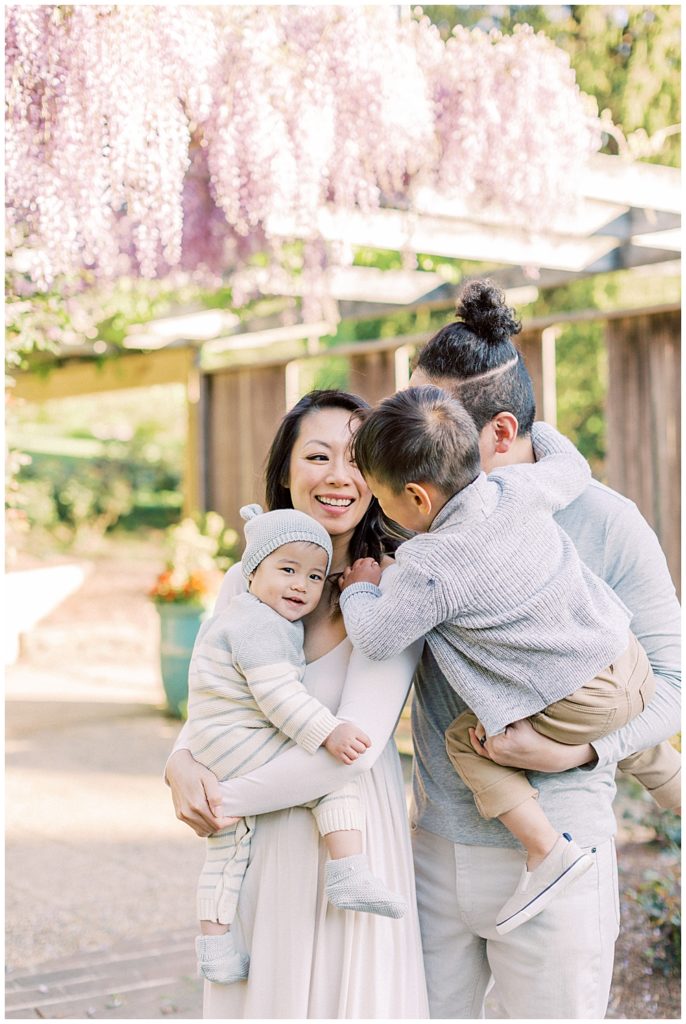 Big Brother Leans Over To His Baby Brother During A Family Photo Session At Brookside Gardens Outside Of Washington, D.c.