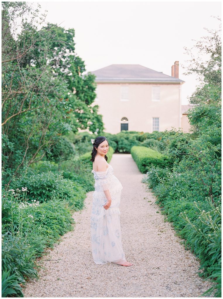 Pregnant Woman Walks Along Path At Tudor House During Maternity Session