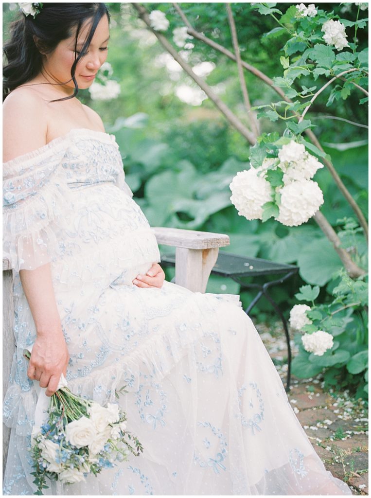 Pregnant Mother Sits On A Bench Near White Flowers At Tudor Place In Dc