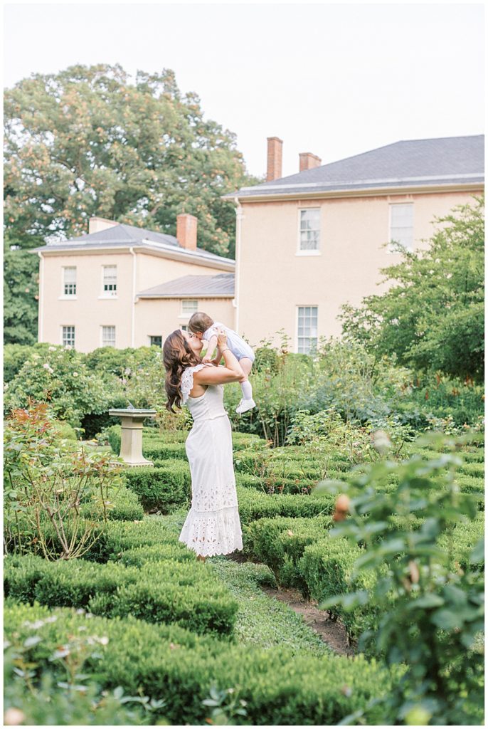 Washington Dc Family Photographer | Mother Holds Her Son Up In The Air In The Gardens At Tudor Place