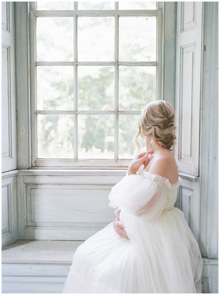 Woman Looks Out A Window, Holding Her Belly