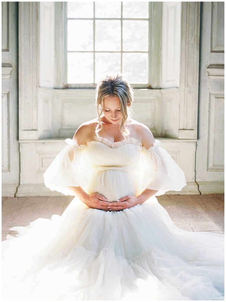 Washington Dc Maternity | Woman Kneels In Front Of The Window, Holding Her Belly