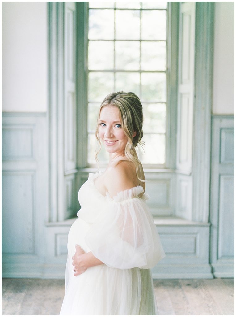 Pregnant Woman Stands With Her Hands Below Her Belly Smiling