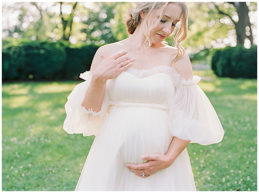 Maternity Session In Northern Virginia At Salubria | Woman Cradles Her Belly And Traces Her Neck With Her Other Hand