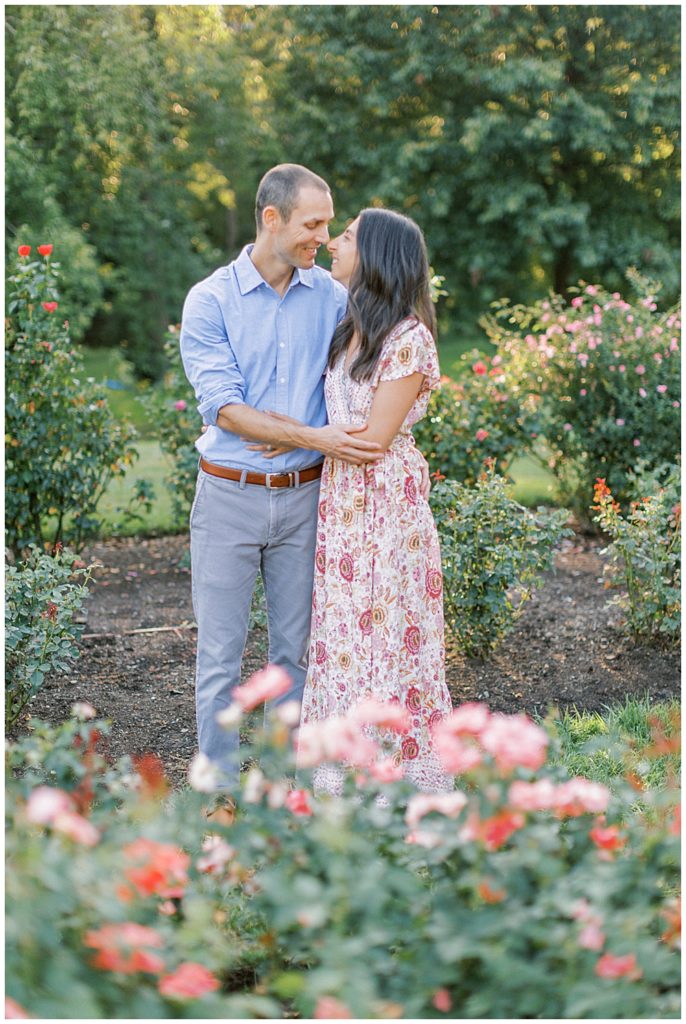 Mother And Father Stand And Hold One Another In A Rose Garden