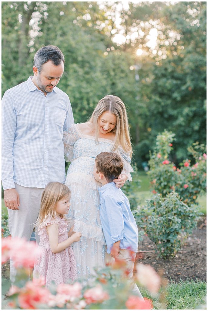 Parents Look Lovingly Down At Their Two Children While Standing In The Bon Air Rose Garden