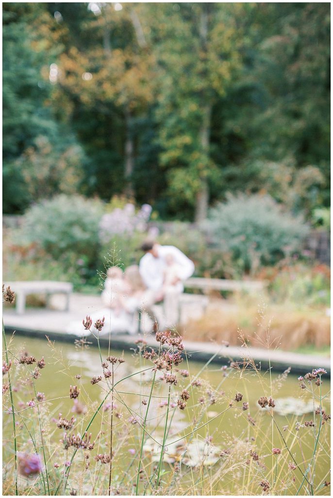 Family Sits By Pond In A Garden