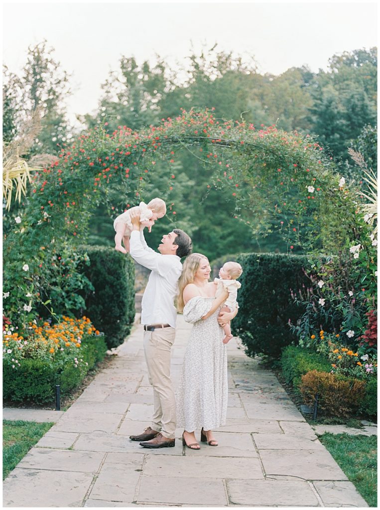 Parents hold twin girls by a floral arch at Brookside Gardens