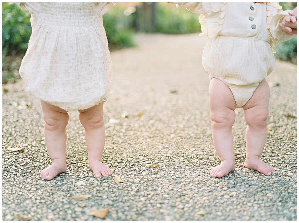 Two Babies Standing Up With A View Of Their Legs During A Twin Family Session At Brookside Gardens