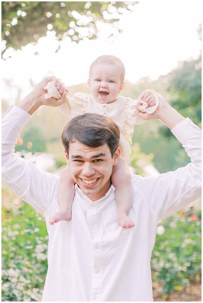 A Baby Sitting On Her Dad's Shoulders Smiling 