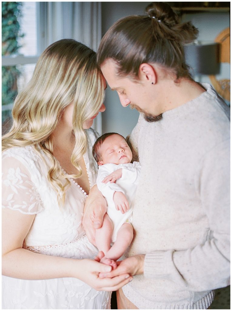 A Mother And Father Face One Another, Holding Their Baby Girl During Their Arlington Newborn Session