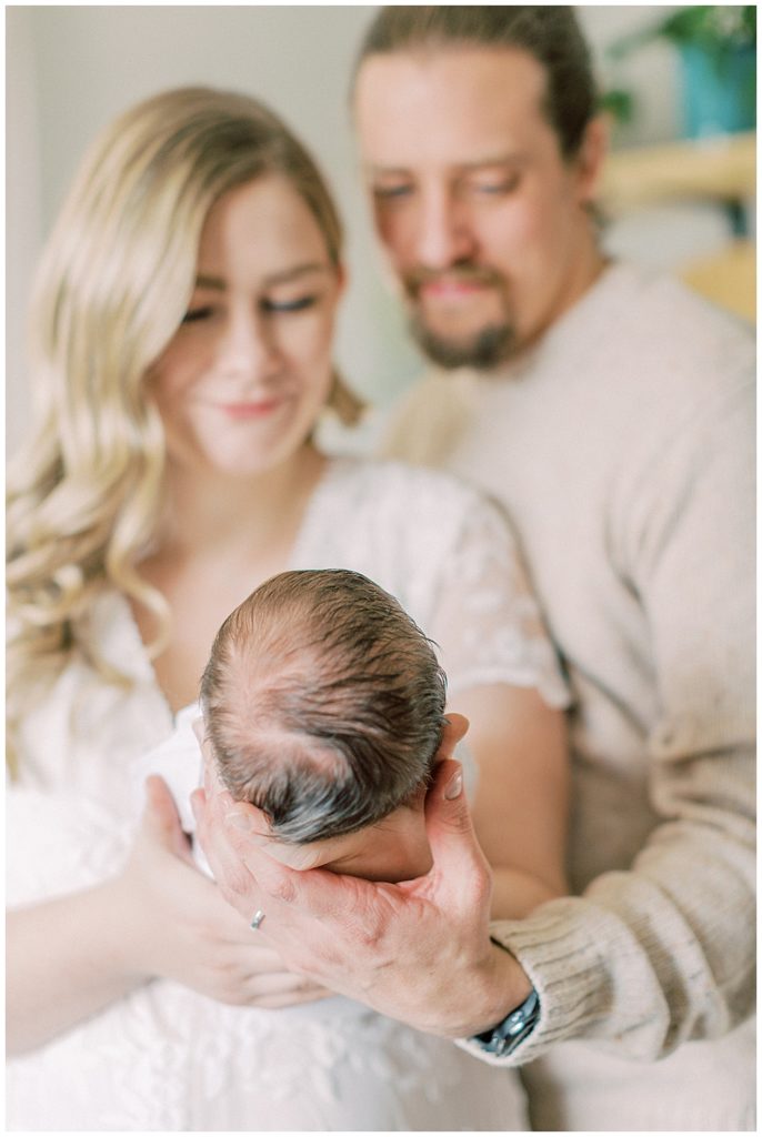 New Parents Hold Their Newborn Out In Front Of Them Looking Lovingly At Her During Their Newborn Session In Arlington