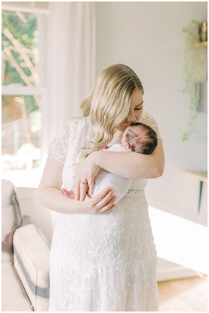 A Blonde Mother Brings Her Baby Girl Up To Her Face To Kiss Her During Their Newborn Session In Northern Va