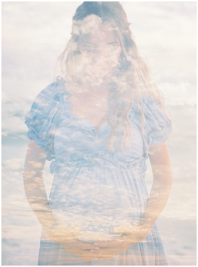 A Double Exposure Of A Mother Wearing A Blue Dress Looking Down At Her Belly And The Sky During A Beach Maternity Photoshoot