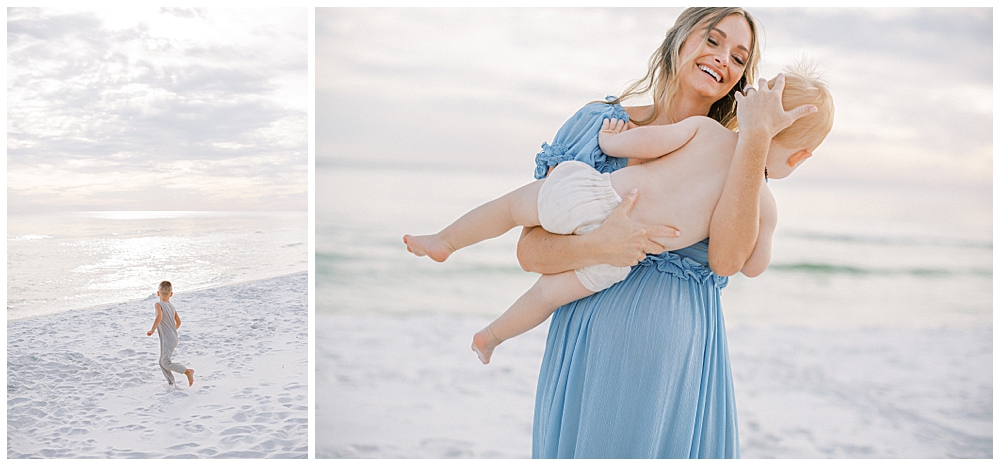 Mother Wearing A Blue Dress Stands On The Beach Holding Her Young Son And Laughing During Her Maternity Session