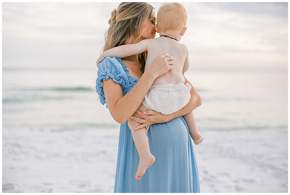 Mother Nuzzles Her Young Son While Holding Him On The Beach