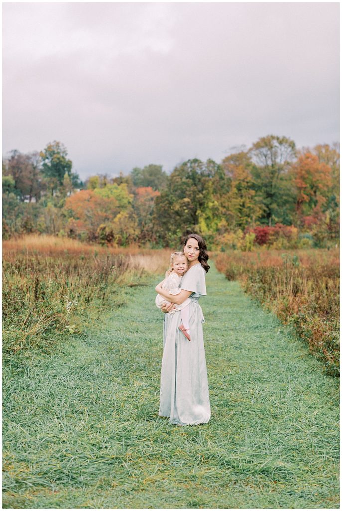 Mother Holds Her Toddler Daughter While Standing In A Clearing At The Howard County Conservancy And Looks At The Camera