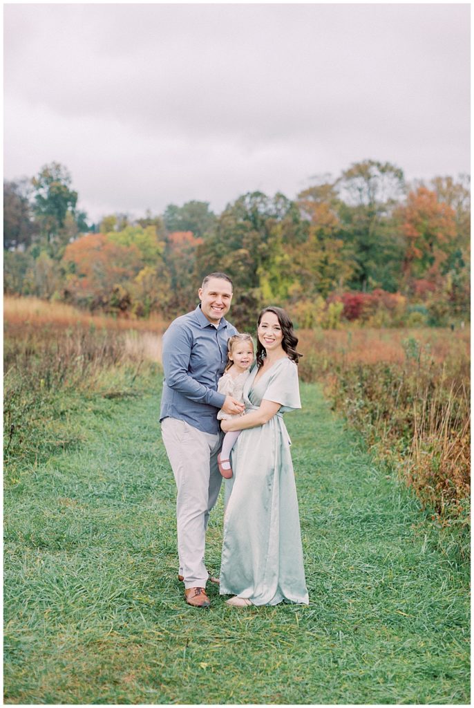 Family Portrait At The Howard County Conservancy Of Mother, Father, And Toddler Daughter Standing In A Clearing