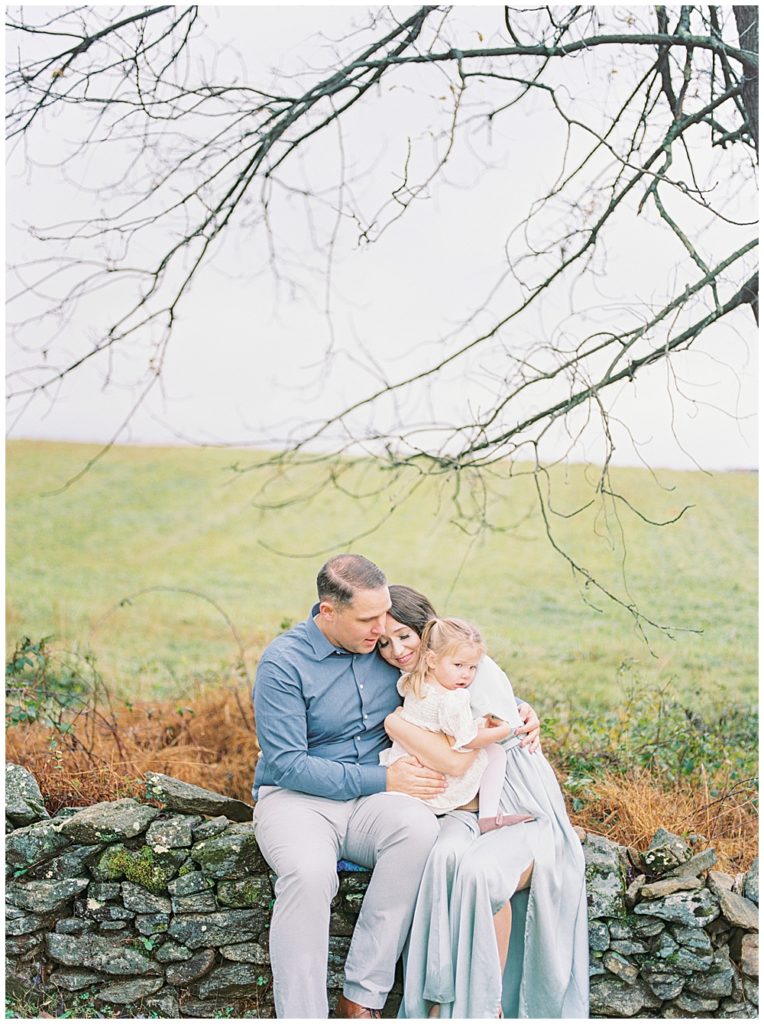 Mother Rests Her Head On Her Husband's Shoulder While They Sit On A Stone Wall At The Howard County Conservancy In Maryland