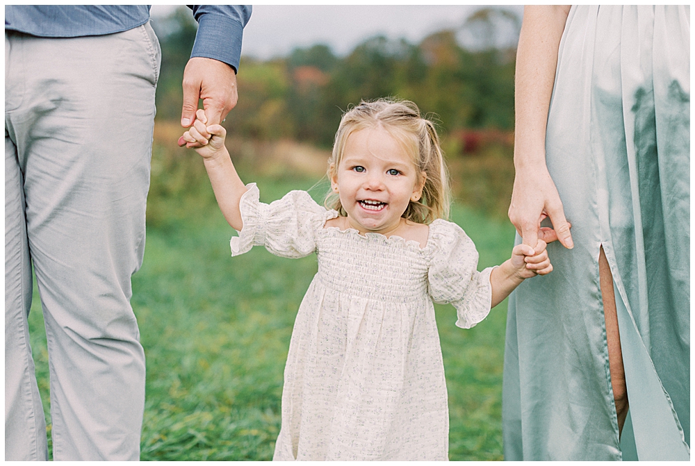 Little Girl Smiles As She Holds Her Mother And Father's Hands At The Howard County Conservancy