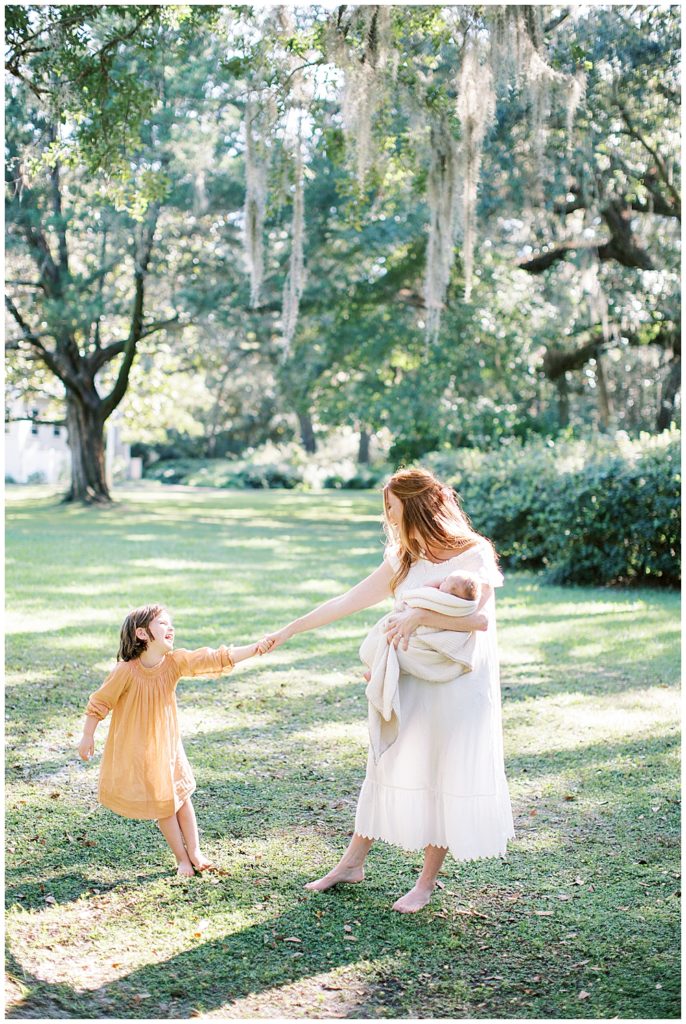 A New Mother Holds Her Daughter's Hand While Her Daughter Gently Pulls Away, All The While The Mother Is Holding Her Newborn