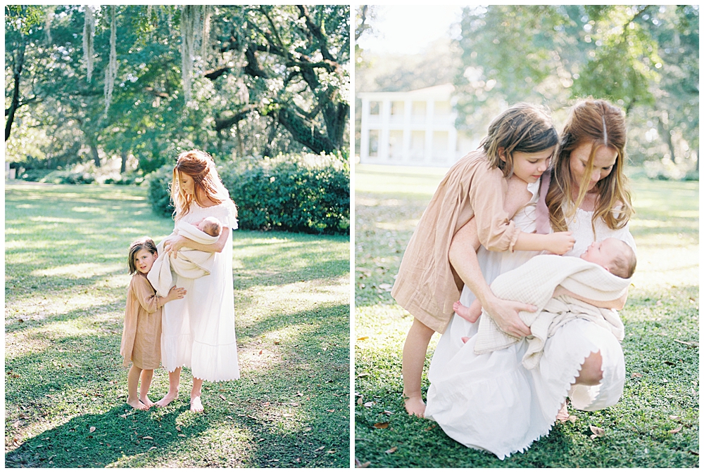 A Little Girl In A Pink Dress With Her Mother In A White Dress Holding Their Newborn Baby Boy During An Outdoor Newborn Session