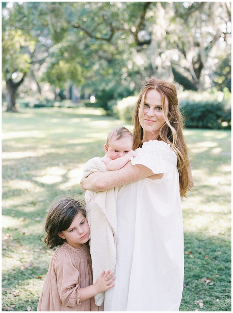 A Red Haired Mother Holds Her Newborn Baby Boy Outside While Her Little Girl Stands Next To Her And Gives Her A Hug