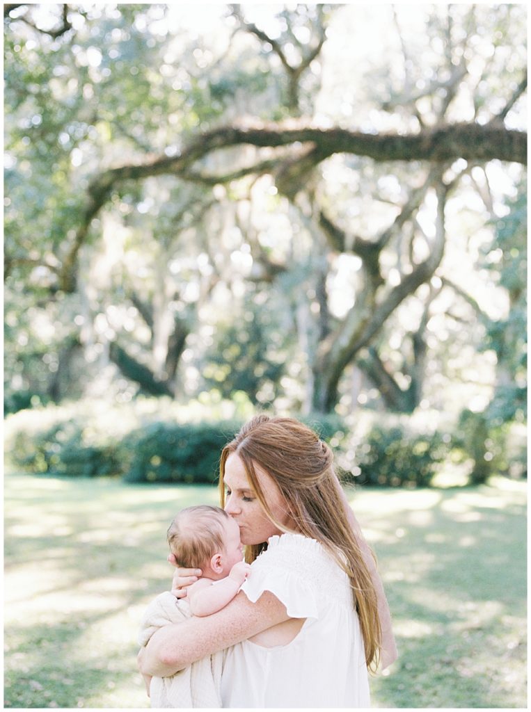 A Red Haired Mother Holds Her Newborn Baby Up To Her Face For A Kiss While Standing Outside Near Spanish Moss