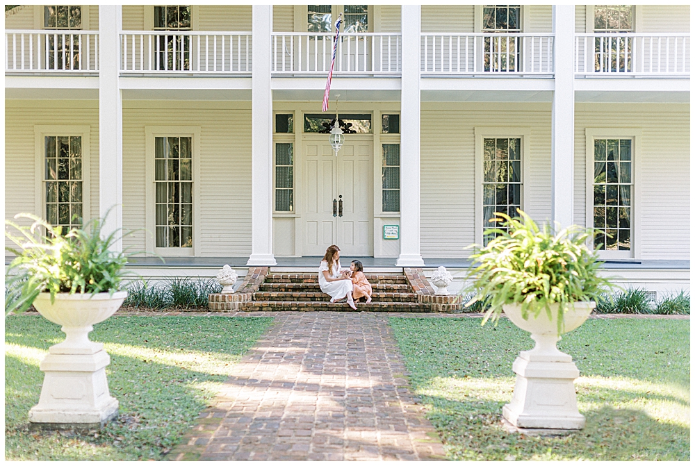 A Mother And Her Young Daughter Sit On The Steps Of A Large Manor During Their Outdoor Newborn Session