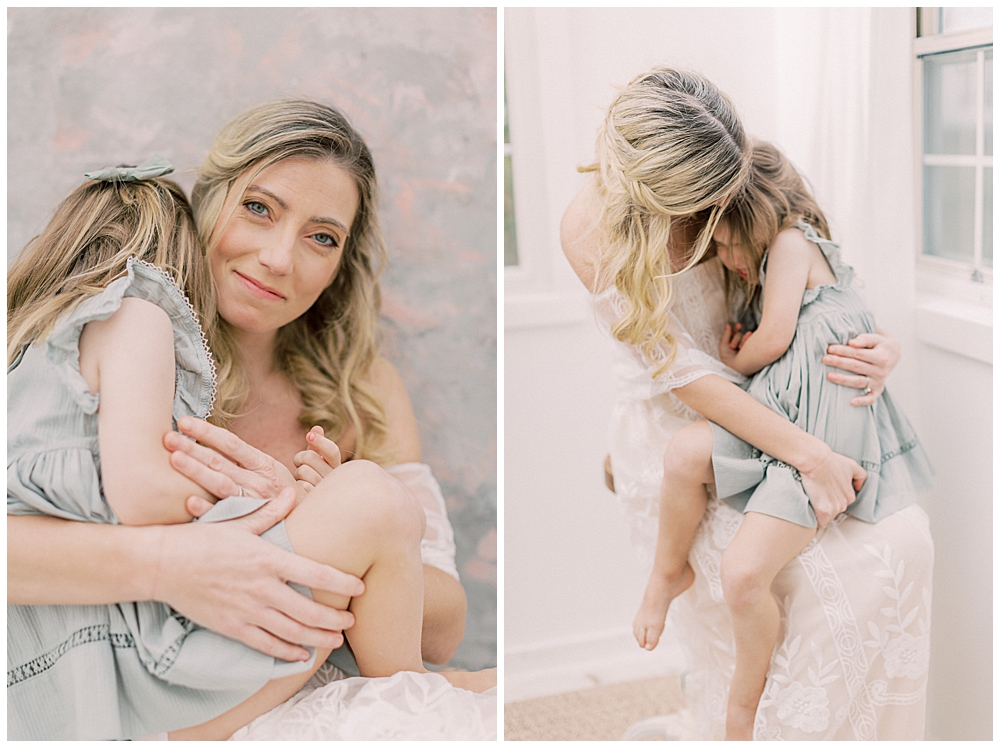 A Studio Motherhood Session With A Mother In A White Dress And Her Young Daughter In A Green Dress Cuddling Together