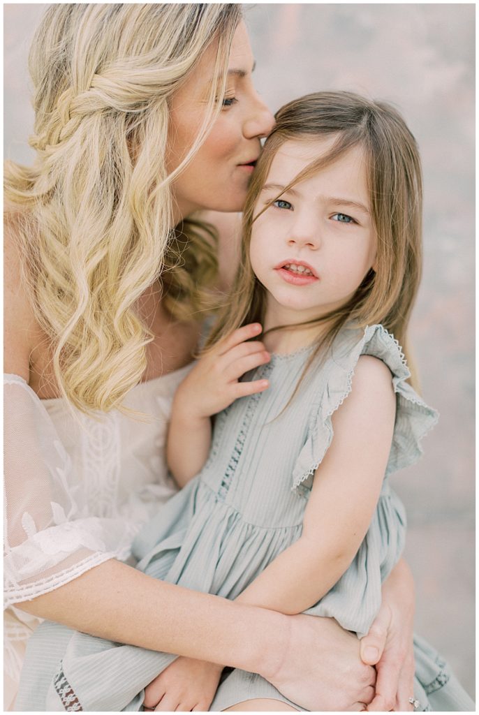 A Mother Kisses The Side Of Her Daughter's Head During Their Studio Motherhood Session