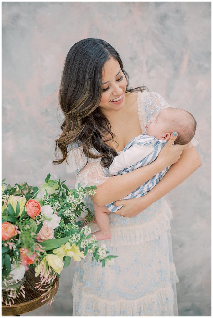 Mother Smiles Down At Her Infant Son While Holding Him 