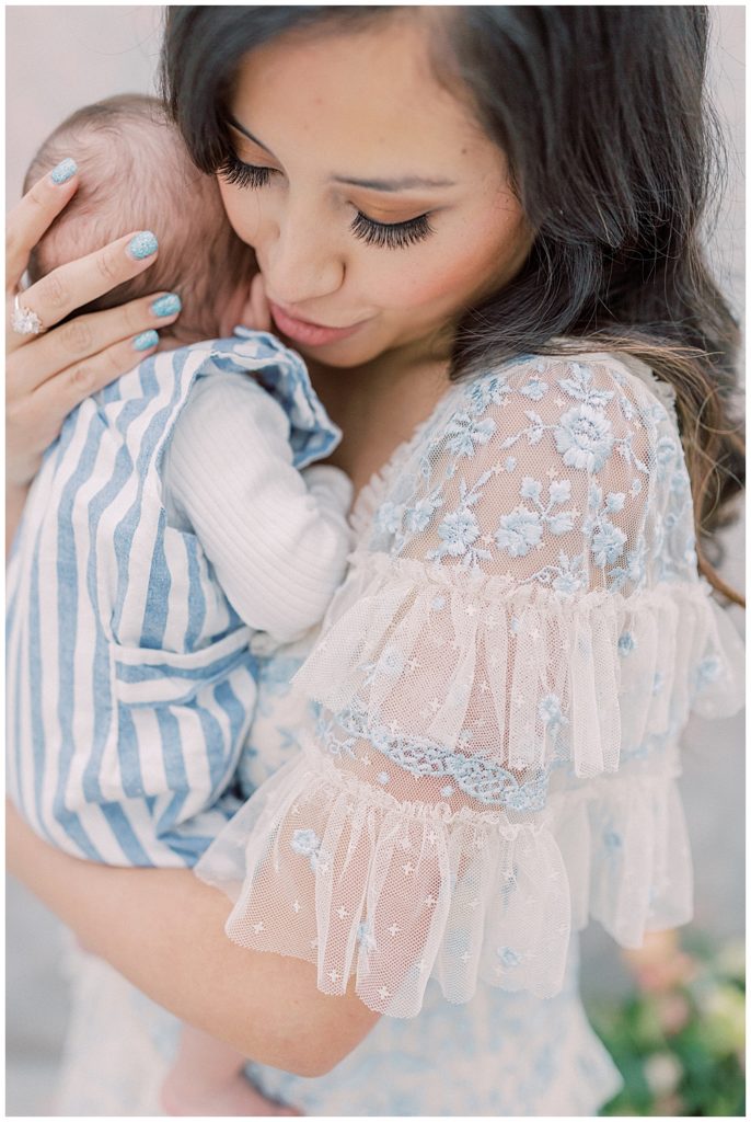 A Mother Wearing A Blue Dress Holds Her Infant Son Up To Her While She Comforts Him