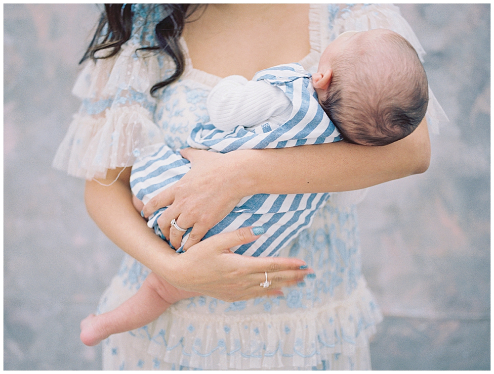 A Mother Holds Her Infant Son Who Is Wearing A White And Blue Striped Onesie